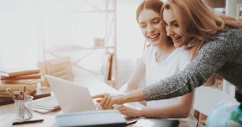 Image of a young student in a white shirt looking at a laptop while taking some pointers from her mom. 